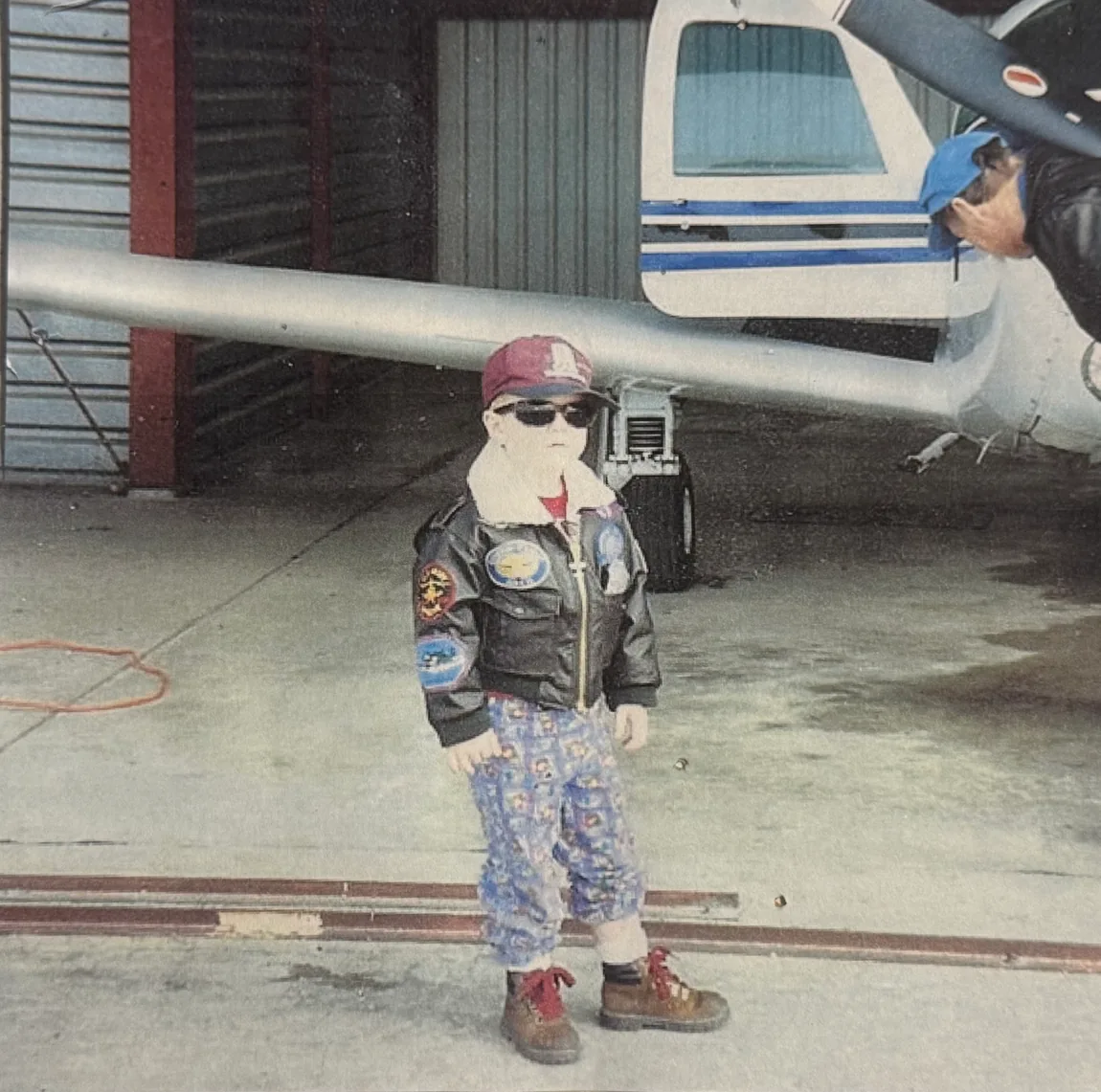 Seth's brother as a child in a leather aviator jacket beside the family Mooney